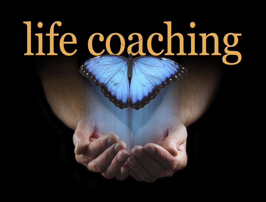 The light touch of a life coach - male hands cupped emerging from a black background with a large blue butterfly rising up towards the words LIFE COACHING